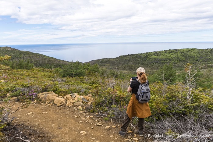 A woman on Green Gardens trail taking photos of the hills and ocean.