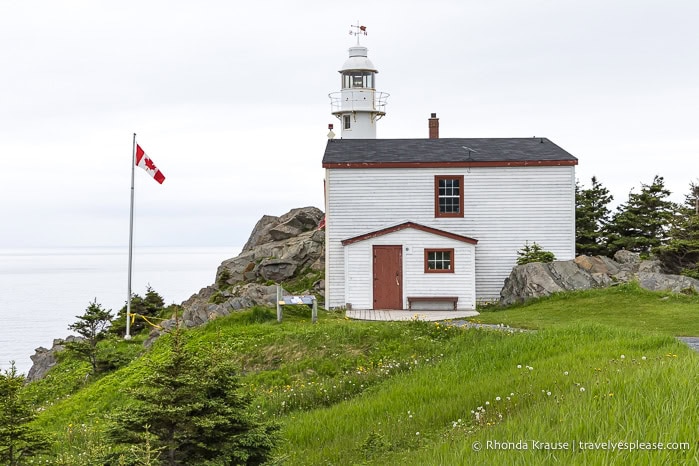 Lobster Cove Head Lighthouse beside a Canadian flag.