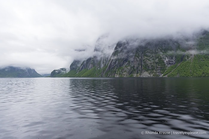 Cliffs beside Western Brook Pond partially covered by low hanging clouds.