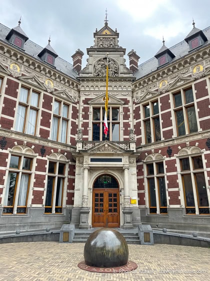 Historic building (University Hall) with a sphere sculpture in front.